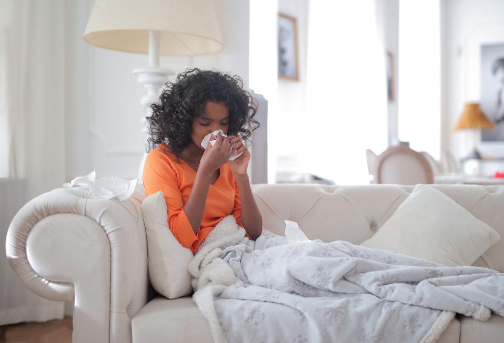 What to do about fall allergies, girl in orange shirt on a tan couch blowing her nose