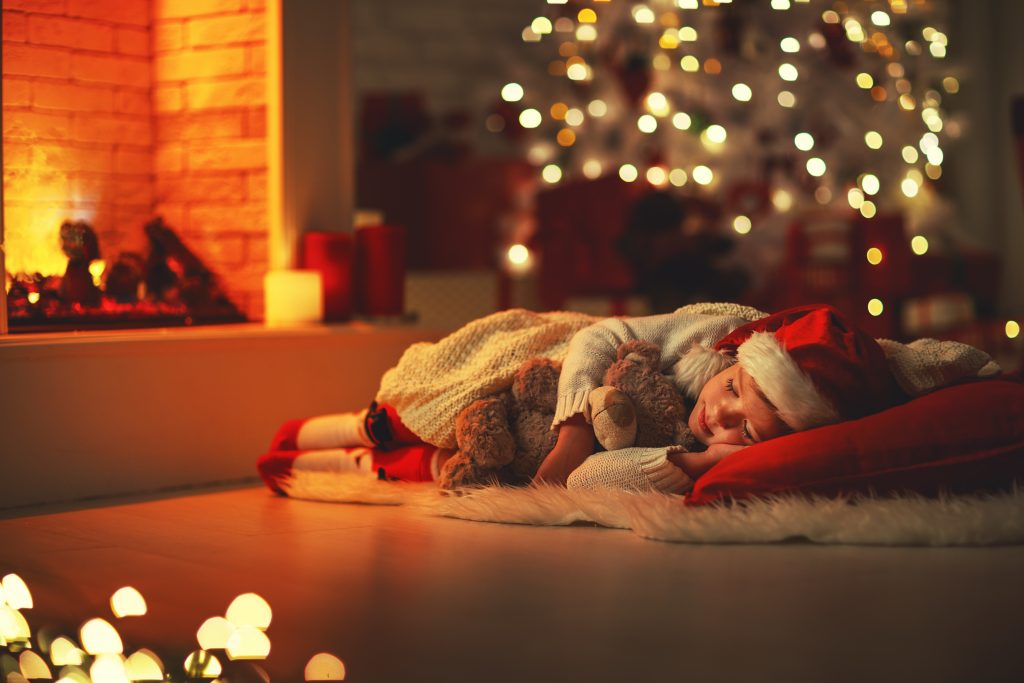 Little girl sleeping next to a fireplace with a Christmas tree in the background