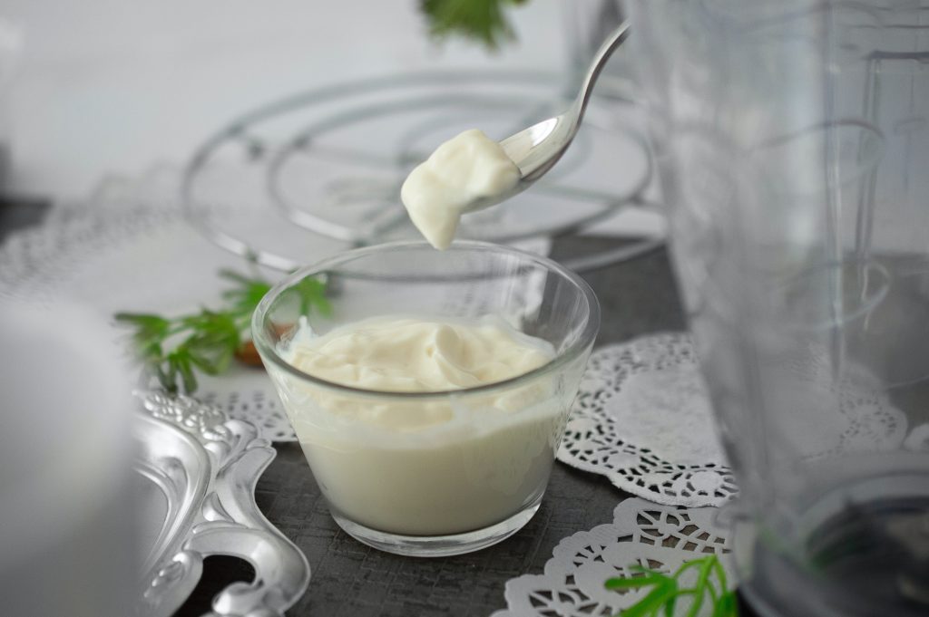 A clear glass bowl holds creamy Greek yogurt, its surface smooth and inviting. A spoon, just dipped into the yogurt, is lifted, carrying a perfect spoonful that hands midair.