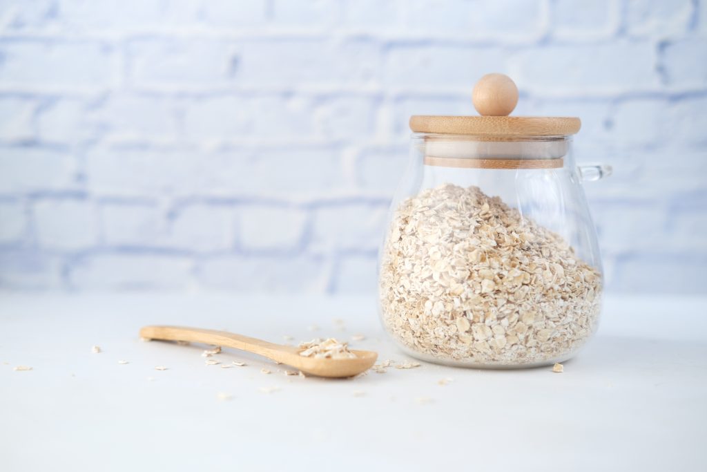 A glass jar filled with wholesome oats stands on a kitchen counter, accompanied by a wooden spoon placed beside it.