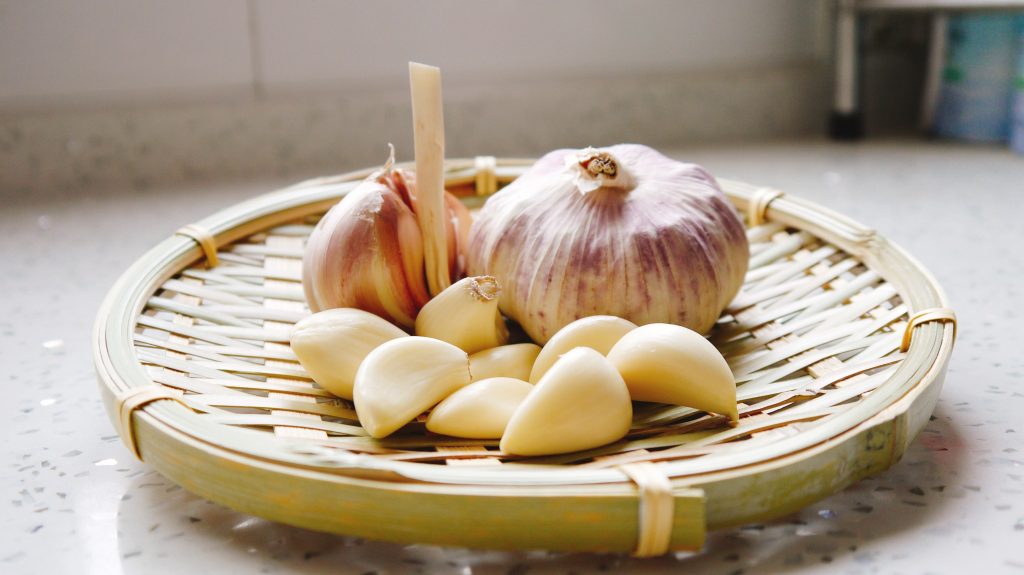 A cluster of cloves of garlic rests in a bowl, situated on a kitchen counter.